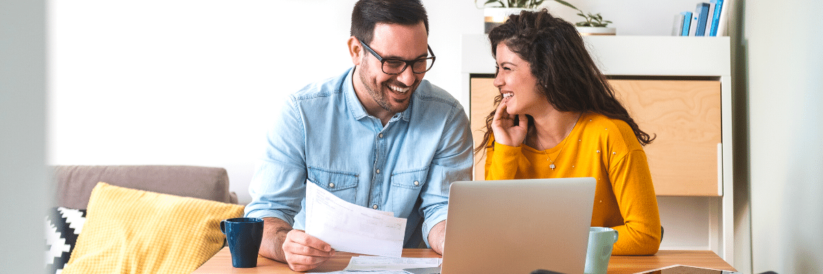 Smiling couple managing finances, reviewing their bank accounts using laptop computer and calculator at modern kitchen